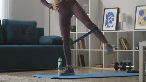 home-gym-in-modern-apartment-woman-is-training-with-elastic-band-on-legs-closeup-view-of-body-parts-healthy-lifestyle